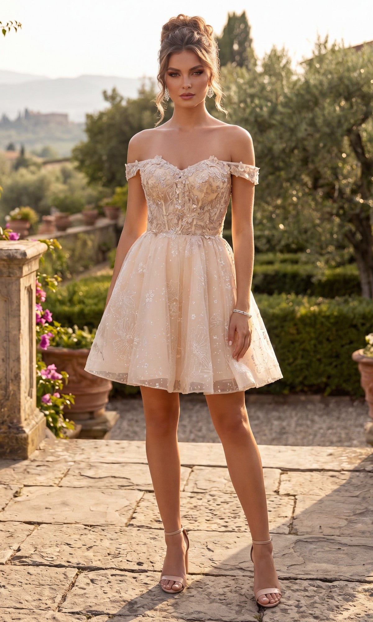 A woman stands outdoors in a garden wearing the Short Homecoming Dress: Chicas C377 in champagne, featuring a short, off-the-shoulder design with floral lace details and an elegant embroidered corset bodice. She pairs the look with high heels, while a stone pathway, lush greenery, and distant hills complete the charming background.